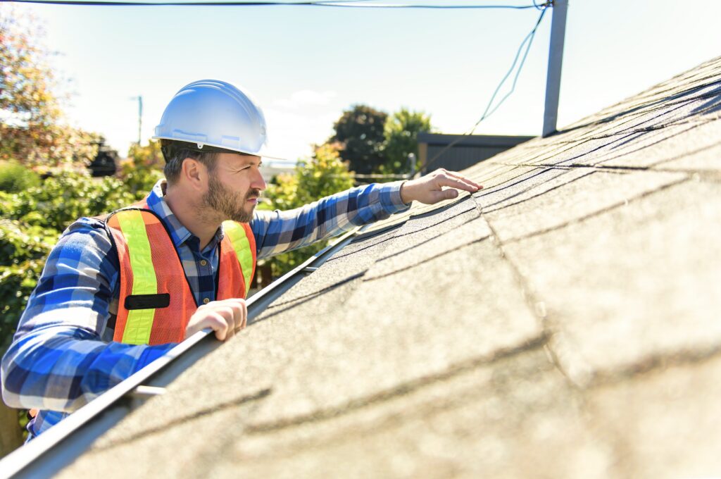 Roofer in a hard hat inspecting an asphalt shingle roof